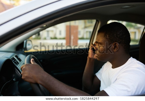 An African man driving a car is talking\
on the phone and looking out the front\
window