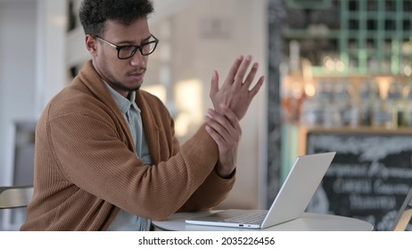 African Man Having Wrist Pain While Using Laptop In Cafe 