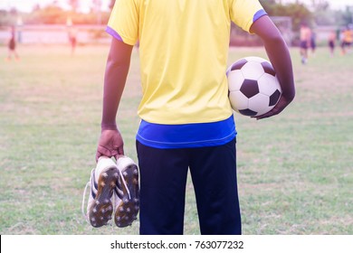 African Man Holding Football Boots And Football Stands Watching Soccer Practice.