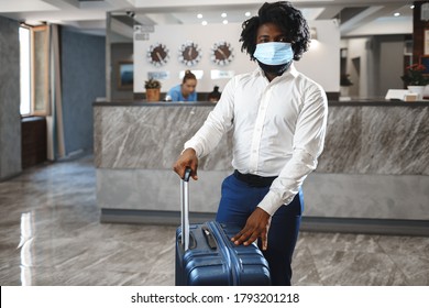 African man hotel guest with suitcase wearing protective mask to protect from coronavirus