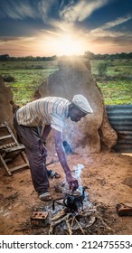 African Man Lifting The Lid From An Old Burned Tea Pot Standing On The Fireplace In An African Village