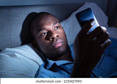 African Man Lying On Bed Using Mobile Phone At Night