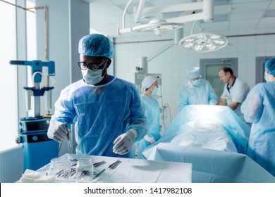 african man in mask and cup taking surgical instruments while operating in a hospital. doctors saving the life of sick man