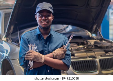African man mechanic in uniform with crossed arms and wrenches standing at the car repair station