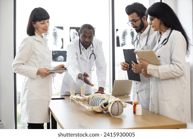 African man medical teacher teaching anatomy to university students or young doctors. Arabian man, Caucasian and Indian women standing near table, working with human skeleton model with body organs. - Powered by Shutterstock