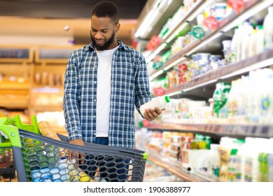 African Man On Grocery Shopping In Supermarket Choosing Dairy Products Buying Food, Standing With Shop Cart Full Of Groceries In Store. Customer In Hypermarket, Coupon And Discount Ad. Free Space