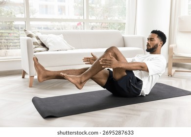 African man performs core exercise, boat pose or bicycle crunch, training abdominal muscles on mat inf sunny living room, strengthening abs muscles, improve balance, enhancing stability, and endurance