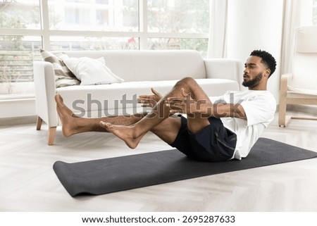African man performs core exercise, boat pose or bicycle crunch, training abdominal muscles on mat inf sunny living room, strengthening abs muscles, improve balance, enhancing stability, and endurance