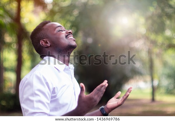 African man praying for thank god with light flare\
in the green nature