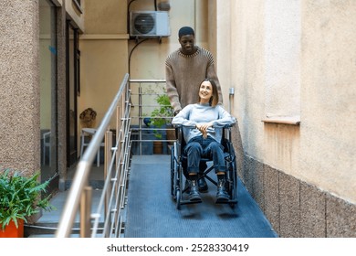 African man pushing the wheelchair of disabled colleague leaving a modern coworking building - Powered by Shutterstock