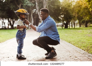 African man putting helmet on cute boy at the park. Father puts his son a protective helmet for riding bike. - Powered by Shutterstock