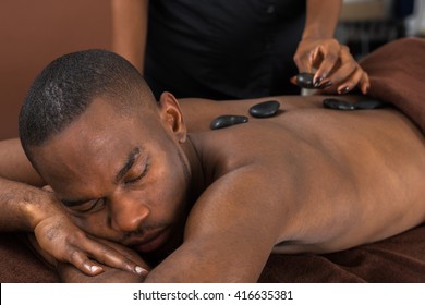 African Man Relaxing In A Spa Getting Hot Stone Therapy