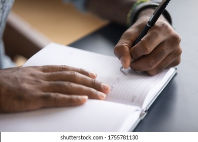 African man sit at desk hold pen keeps startup business ideas, plans, creative thoughts to notebook close up image. Makes appointment notes time, writes important things and to-do list not to forget