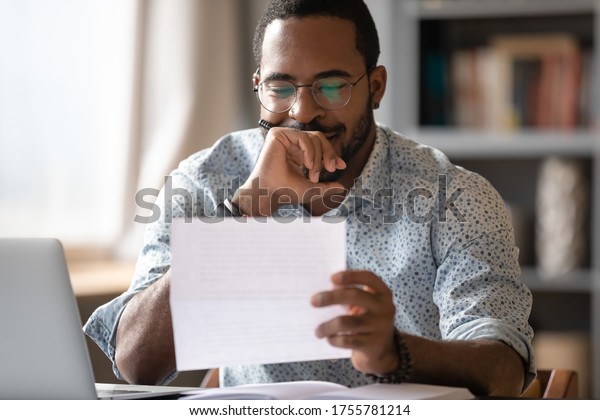 African man sit at desk hold postal\
correspondence letter read good news feel proud by personal\
business achievement, got hired, receive reward, financial success\
statement, approved bank loan\
concept