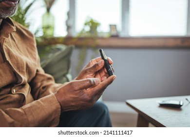 A African Man Sits At A Table In The Living Room And Takes Blood From His Finger Due To Diabetes. Everyday Life Of A Man Of African American Nationality With A Chronic Disease 