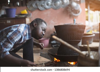 African man sitting to blow fire to cook rice