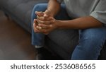 An african man sitting indoors, hands clasped in a relaxed posture on a sofa in a living room setting