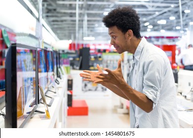 African Man Standing In Front Of A Stand In An Electronics Store, Choosing A Large Plasma TV. Side View