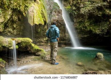 African Man Standing With Wet Rain Jacket In Waterfall Canyon. Hinanger Wasserfall, Allgau, Bavaria, Germany. 