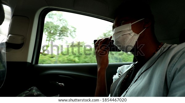 African man in taxi using cellphone\
device listening to audio message during\
pandemic.