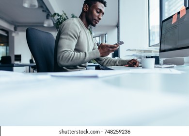 African man using smart phone while sitting at work place. Businessman sitting in modern office. - Shutterstock ID 748259236