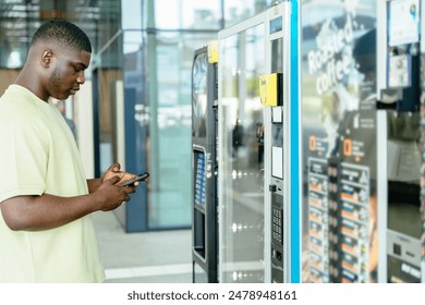 African man using smartphone while standing in front of a vending machine.