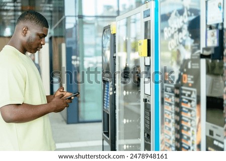 African man using smartphone while standing in front of a vending machine.