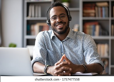 African man wear headset sit at workplace desk smile looking at camera, company consultant portrait, distant communication with client. Easy interesting e-learn study, online modern app usage concept
