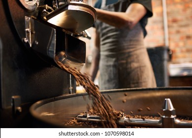 African man wearing an apron busy pouring coffee beans from the coffee roasting machine over to the tray that stirs the beans until they are cool enough to be packaged. - Powered by Shutterstock