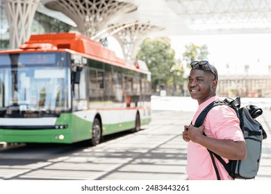 African man wearing a backpack stands in front of a green and white bus wait at bus stop. - Powered by Shutterstock