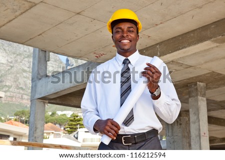 African man wearing a hard hat in a construction site holding building plans