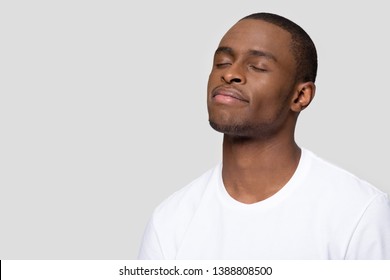 African man wearing white t-shirt closed eyes pose aside isolated on grey blank copy space for creative thoughts advertisement text, guy dreaming feels calmness placidity balance and harmony concept
