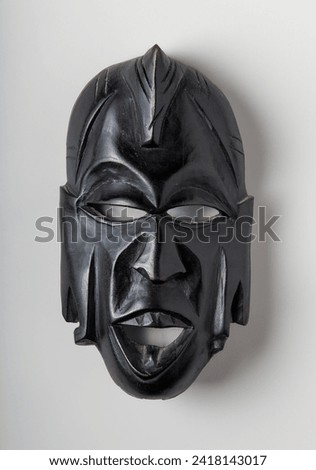 African mask carved in black painted wood on white background vertically