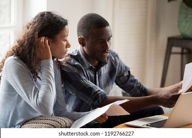 African Millennial stressed married couple sitting on sofa at home checking unpaid bills, taxes, due debt, bank account balance. Bankruptcy, debt and lack of money financial problems in family concept