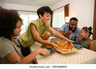 African Mixed Race Family Parents And Two Little Daughter Eating Fried Chicken And Pizza For Dinner Together. Father And Mother And Cute Child Girl Kid Enjoy Eating And Sharing A Meal Together At Home