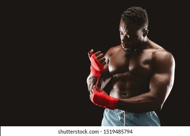 African mma fighter preparing for training, wrapping hands with red bandage, black studio background, copy space - Powered by Shutterstock