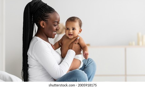 African Mother And Baby Portrait. Profile Side View Of Happy Black Mommy Holding And Playing With Her Adorable Little Infant In Diaper, Free Copy Space, Banner, Selective Focus, Blurred Background