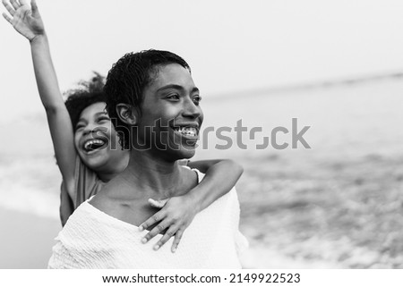 African mother and daughter running on the beach during summer vacation - Focus on mom face - Black and white editing