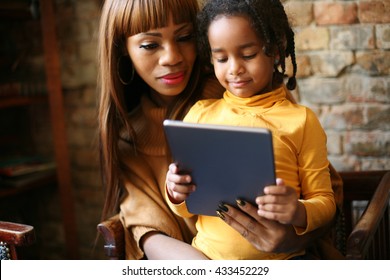 African mother with her smiling daughter using digital tablet at home. 