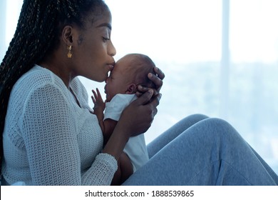 African Mother Holding And Kissing Her 21 Days Baby Boy While Sitting On Bed At Home, Mother And Little Kid Relaxing At Home