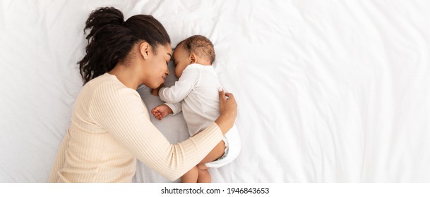 African Mother Hugging Sleeping Baby Lying In Bed Indoor, High Angle Shot. Loving Mom And Toddler Infant Napping Resting During Daytime Sleep. Panorama, Free Space For Text