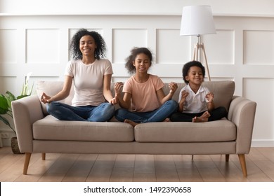 African Mother Little Son Pre-teen Daughter Sit On Sofa In Lotus Pose Doing Yoga Practise Meditation, Yogini Woman Mom Teach To Kids Reach Zen, Funny Activities At Home, Mental Physical Health Concept