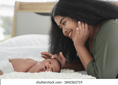 African Mother And New Born Baby In Diaper On A White Bed. Young Mom Smile Touching And Looking At Her Little Infant Boy Sleeping On Bed At Bedroom