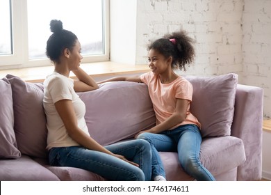 African Mother And Pre-teen Daughter Sitting Together On Sofa Having Honest Pleasant Conversation. Concept Of Trusting Relationship Between Kid And Parent, Gossips Secrets Sharing, Heart-to-heart Talk