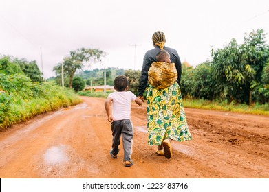 African Mother And Two Children Walk Alone In Red Clay Road In  Village As A Family In Traditional Dress