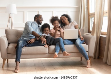 African mother using pc pre-teen daughter having fun online holds smartphone toddler son enjoy tablet computer activity father in glasses hold in hand cell phone, family addicted with gadgets concept