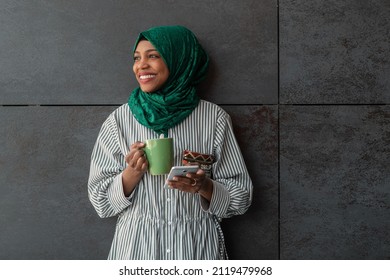 African Muslim businesswoman with green hijab using mobile phone during coffee break from work outside - Powered by Shutterstock