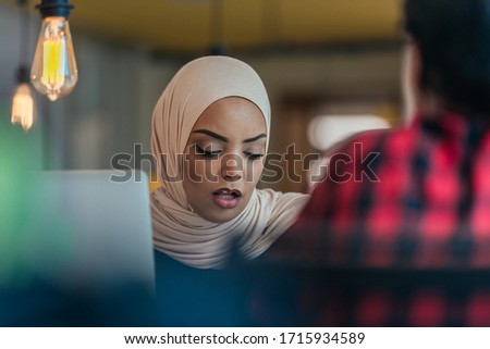 African muslim girl wearing hijab working on a laptop in a modern startup company.