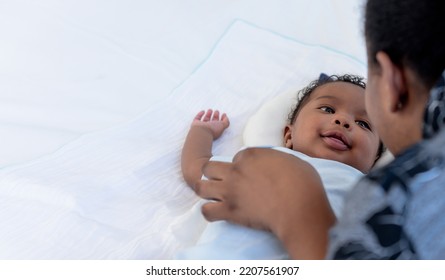 An African Newborn Baby Is 2 Months Old Lying On A White Bed Smiling Happily When He Is Looking At His Mother, To Relationship In African Family And Black Newborn Concept.