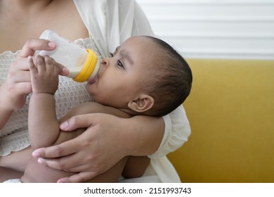 African newborn baby sucking milk from bottle and holding mother finger while lying in young mother arm with tear drop from eye. Caring for a hungry baby concept